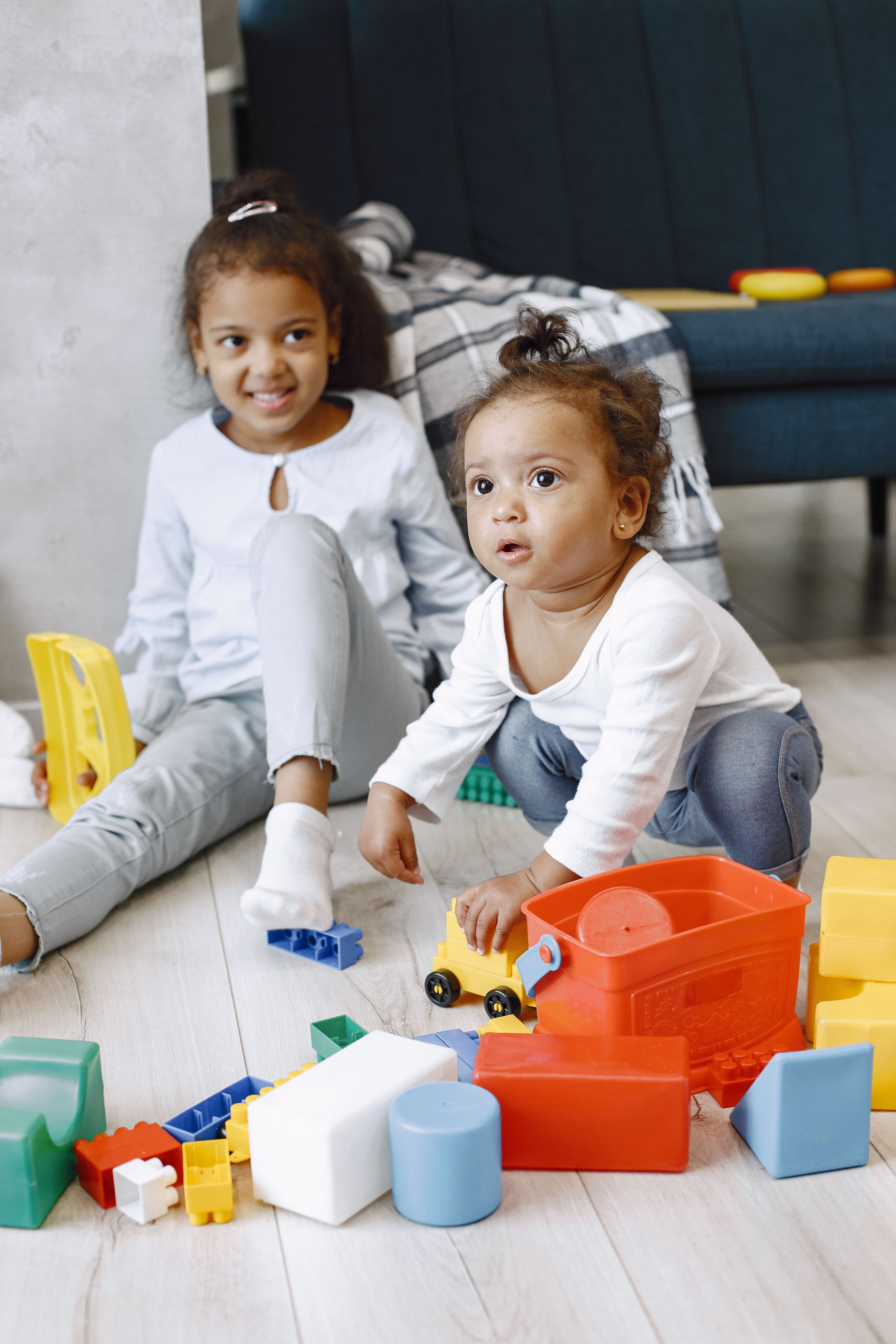Two young children playing with colorful building blocks on a wooden floor