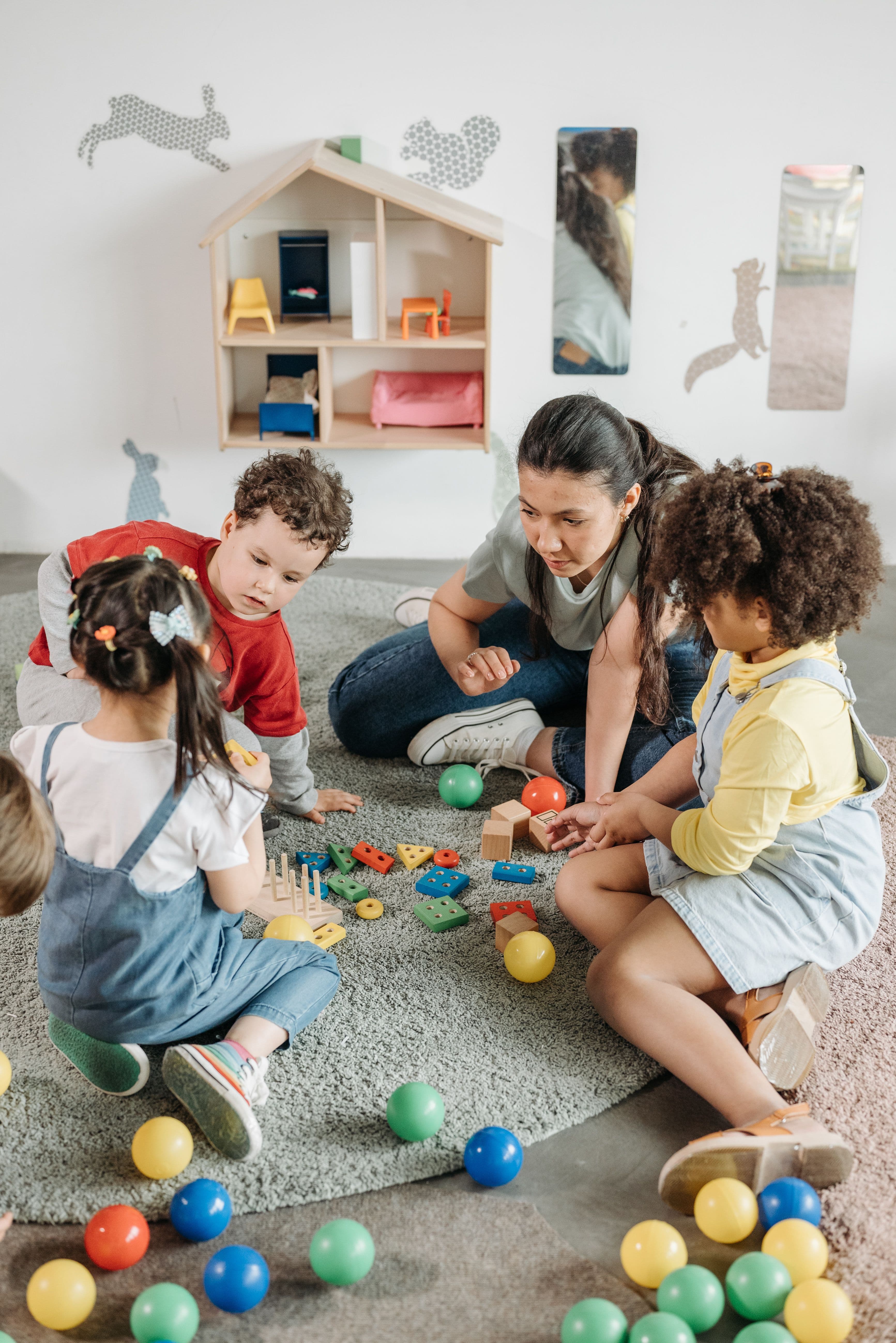 Educator sitting with toddlers exploring toys on a playroom rug